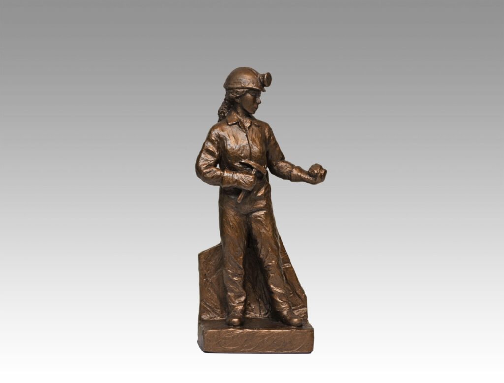 Gallery, Chipping Away, $225 CAD, Metal Infused, 10” H, Edition 80, Mining Sculpture of a Woman Miner holding a chipping hammer and rock with headframe in back, Sculptor Tyler Fauvelle